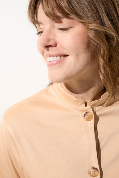 Femme souriante portant un cardigan anti-UV beige avec boutons, tissu léger et élégant, idéal pour le soleil.