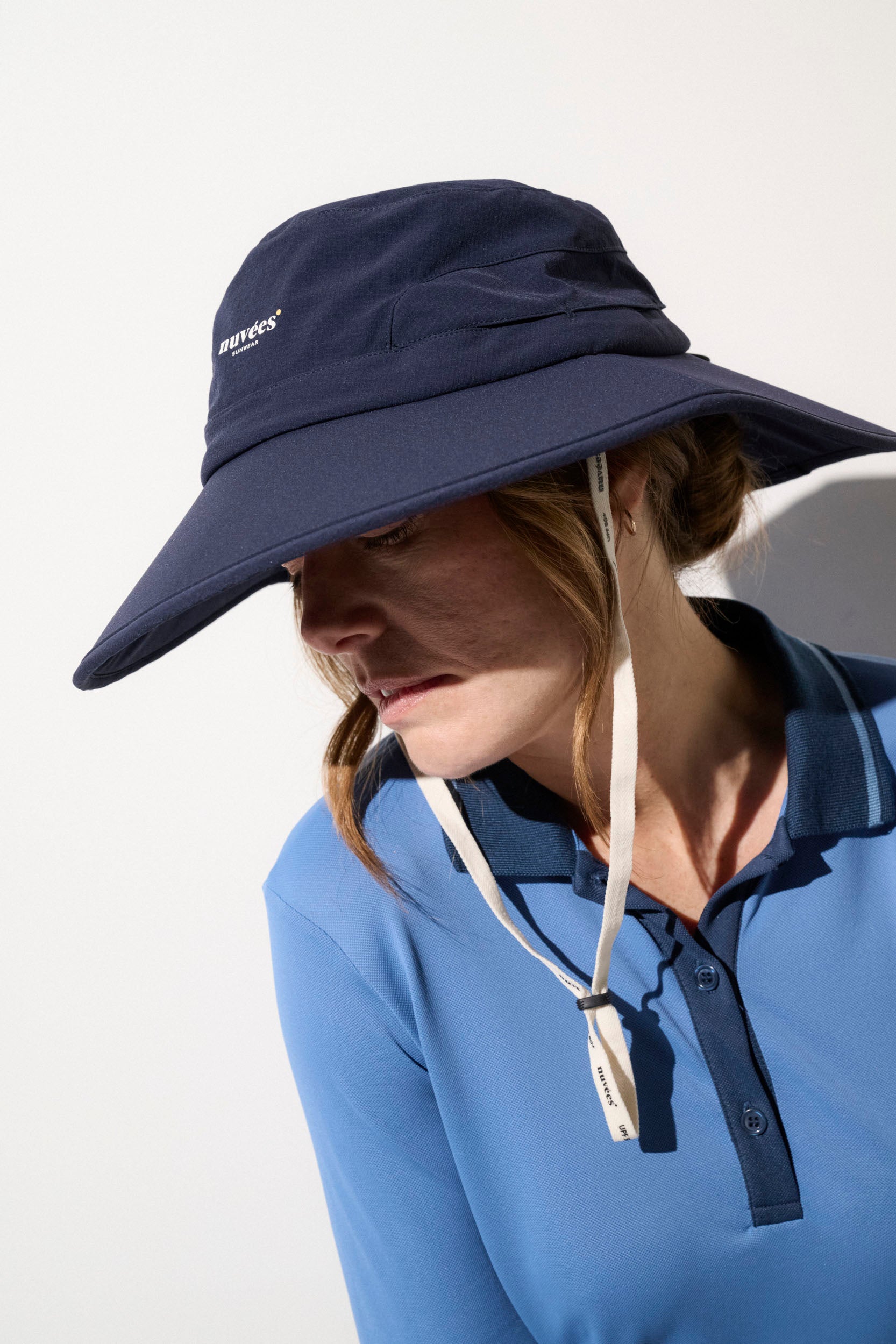 Femme portant un chapeau anti-UV bleu avec protection UPF50+, idéal pour le golf et les activités de plein air.