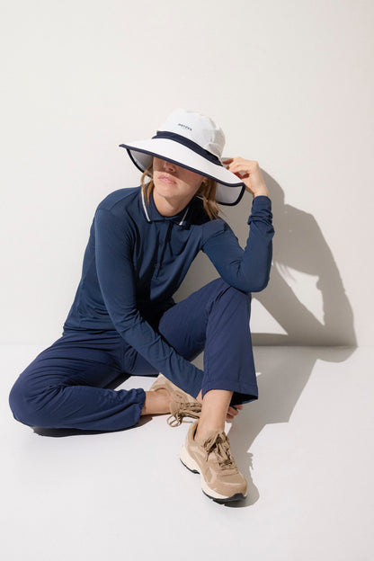 Femme portant un chapeau anti-UV blanc et une tenue légère de sport en bleu, offrant protection solaire UPF50+.