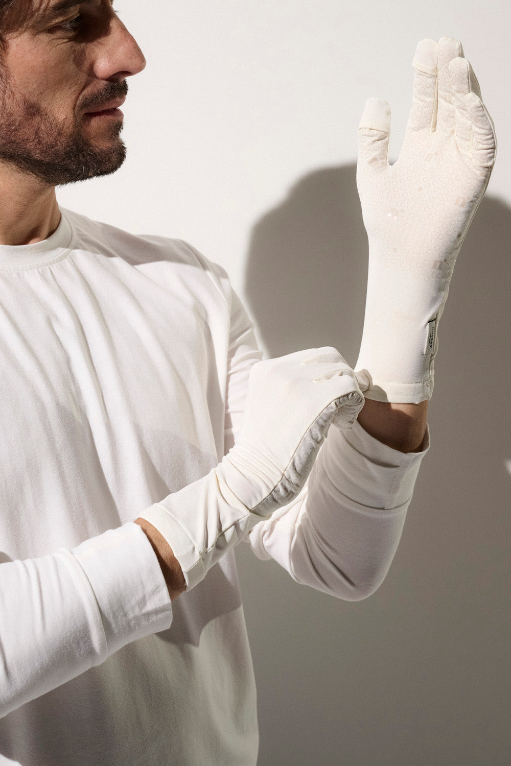 Homme mettant des gants anti-UV blancs UPF50+, pratique pour protection solaire en extérieur.