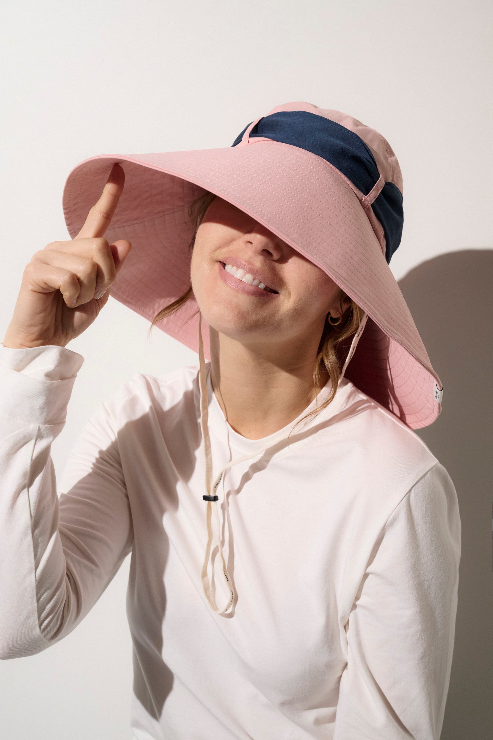 Chapeau anti-UV rose et bleu UPF50+ porté par une femme, idéal pour activités extérieures et protection solaire.