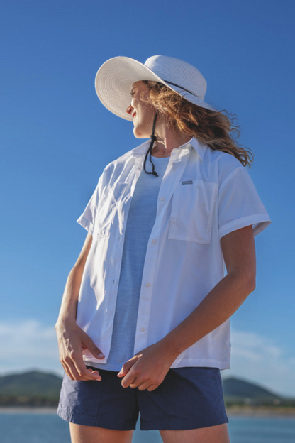 Femme portant une chemise anti-UV blanche UPF50+ et un chapeau, idéale pour la protection solaire en extérieur.