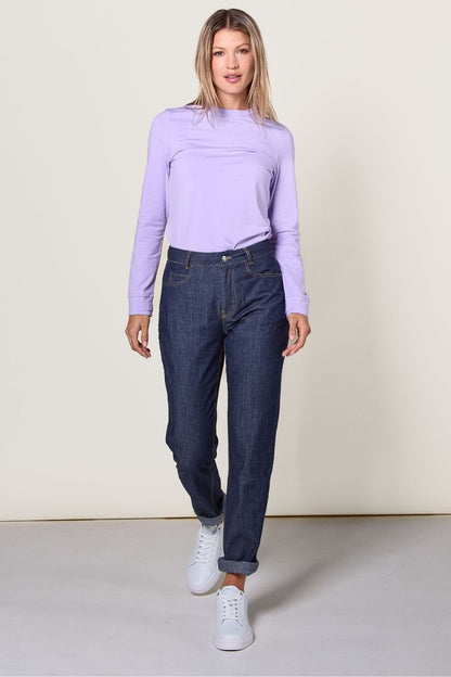 Femme portant un pantalon anti-UV en denim foncé, certificé UPF 50+, associé à un haut violet, idéal pour la protection solaire.